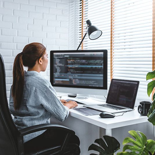 Person working at a desk with multiple computer screens, focused on coding.