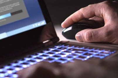 A hand using a computer mouse over a glowing laptop keyboard.