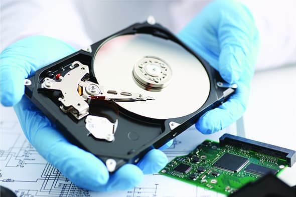 A person in blue gloves holds an open hard drive with visible components.