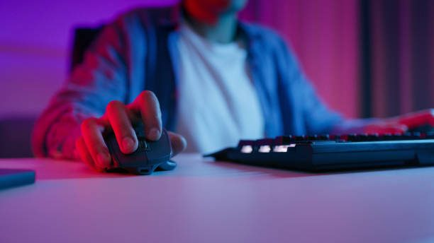 Person using a computer mouse with a keyboard in a dimly lit, colorful room.