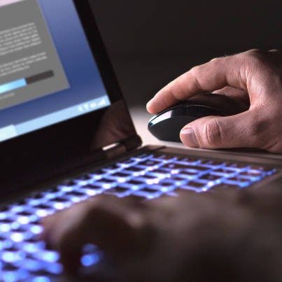 A person using a laptop with a visible illuminated keyboard and a computer mouse.